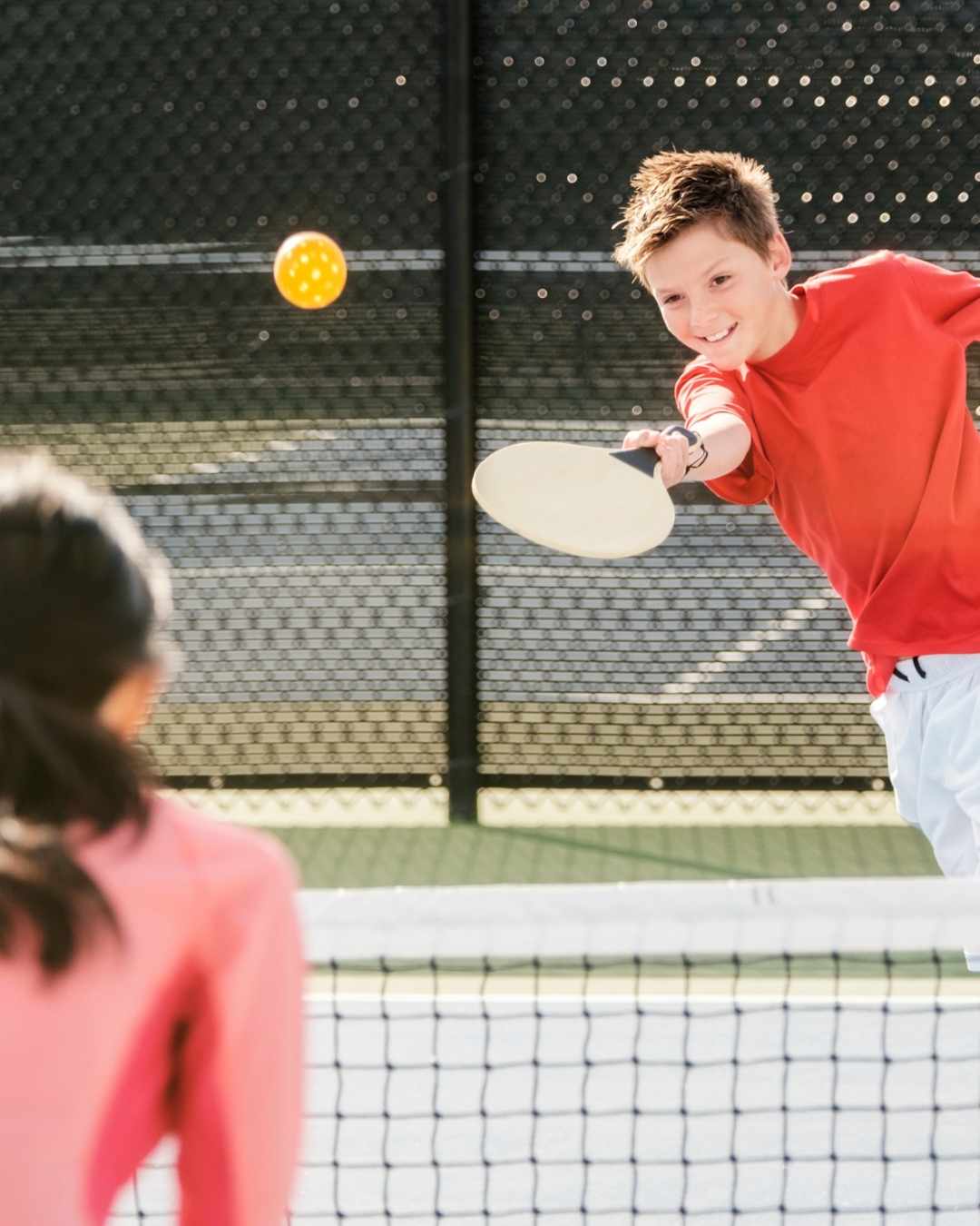Home 3 Enfants en plein apprentissage du pickleball avec des balles colorées sur un terrain extérieur