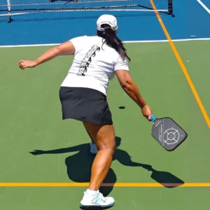 Personne en position basse renvoyant une balle de pickleball sur un terrain extérieur