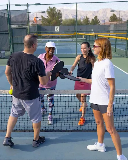 Quatre personnes se saluent au filet en joignant leurs raquettes sur un terrain de pickleball extérieur