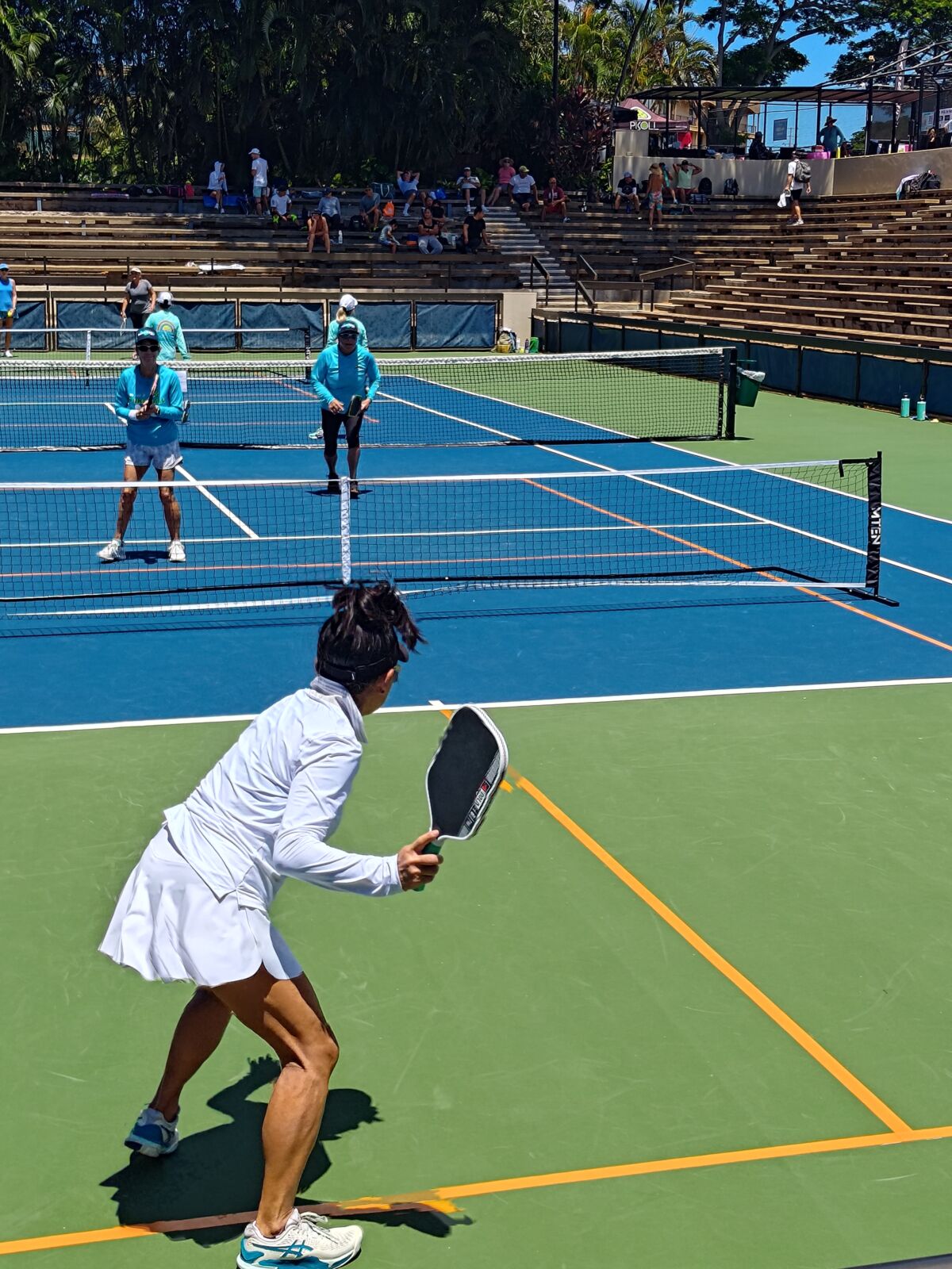 Partie de pickleball sur un terrain extérieur avec public