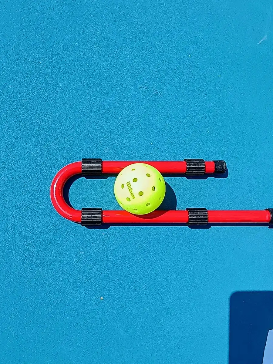Balle de pickleball posée sur un mini-filet rouge sur un court bleu à Aix-en-Provence