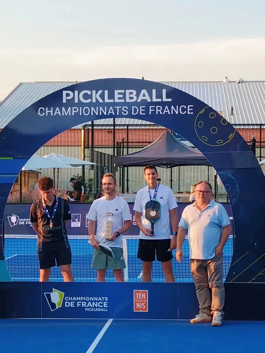 Portrait serré de trois médaillés sous l'arche des Championnats de France de pickleball 2026