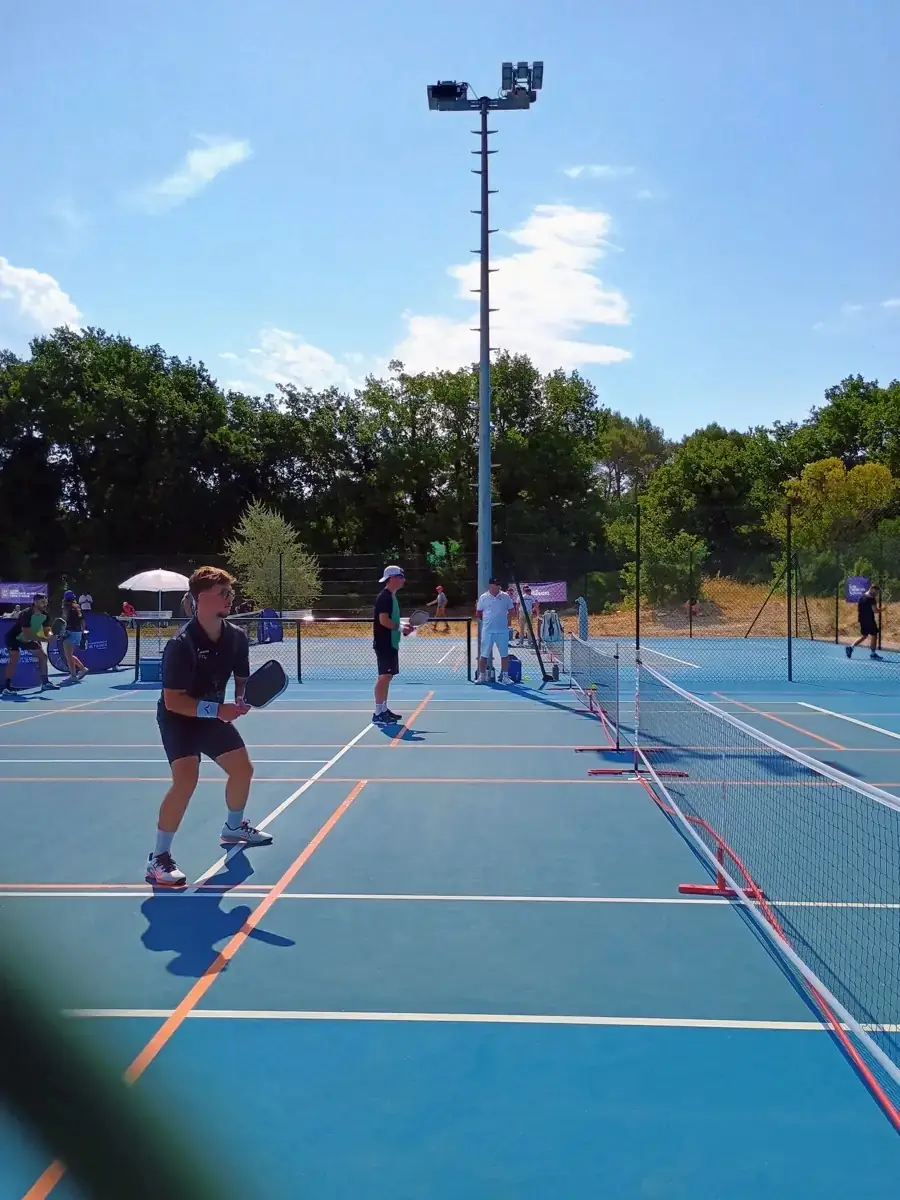 Joueuse sur un terrain extérieur vue à travers le grillage des Championnats de France de pickleball 2026