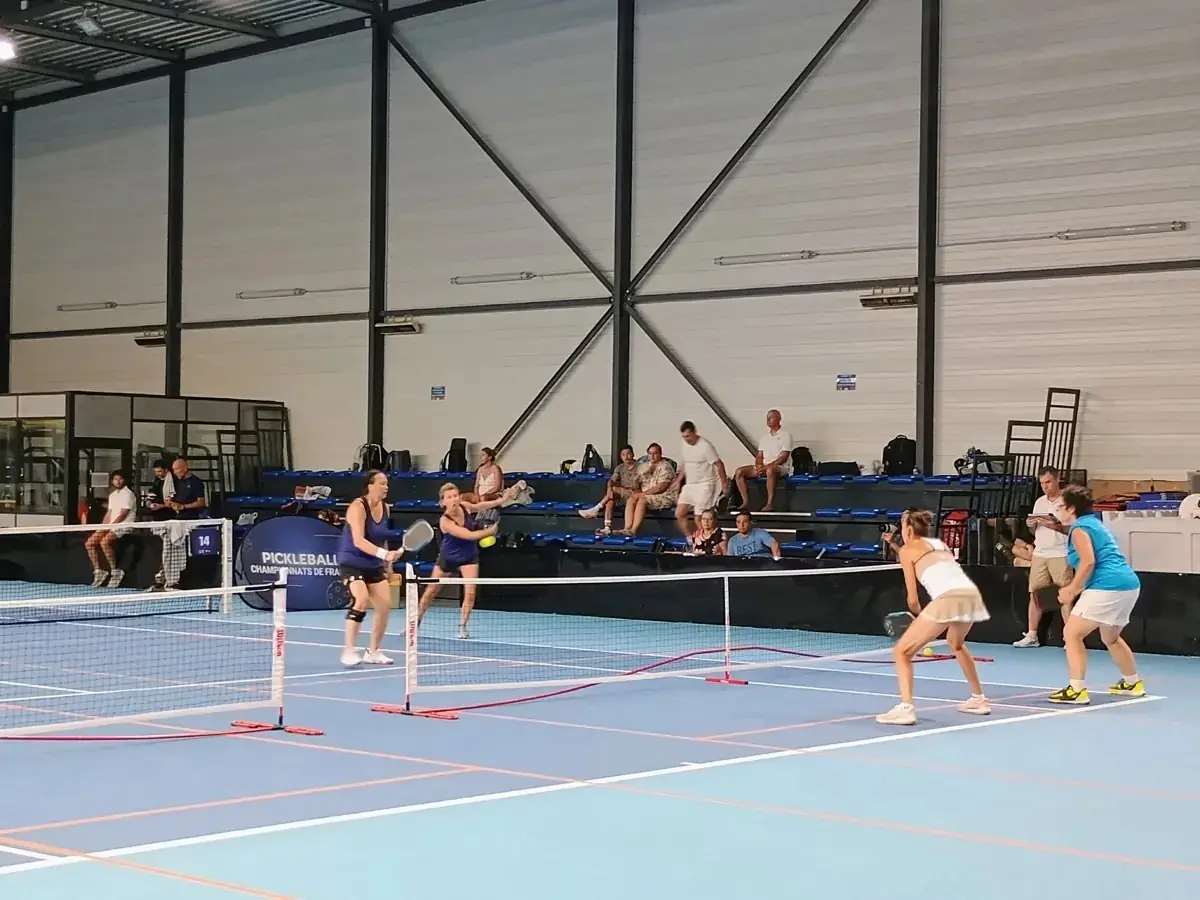Échange en double dans la halle intérieure avec du public au fond aux Championnats de France de pickleball 2026