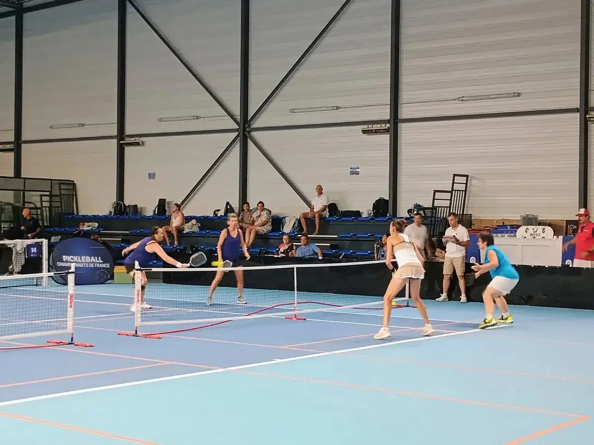 Match sur un terrain intérieur des Championnats de France de pickleball 2026 vu depuis le côté de la halle