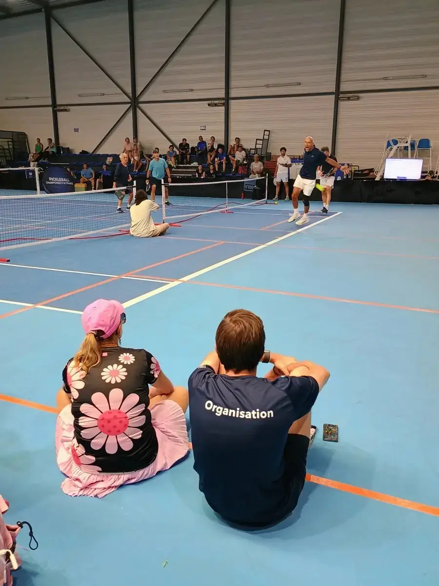 Deux personnes assises au bord d’un terrain dans la halle intérieure des Championnats de France de pickleball 2026