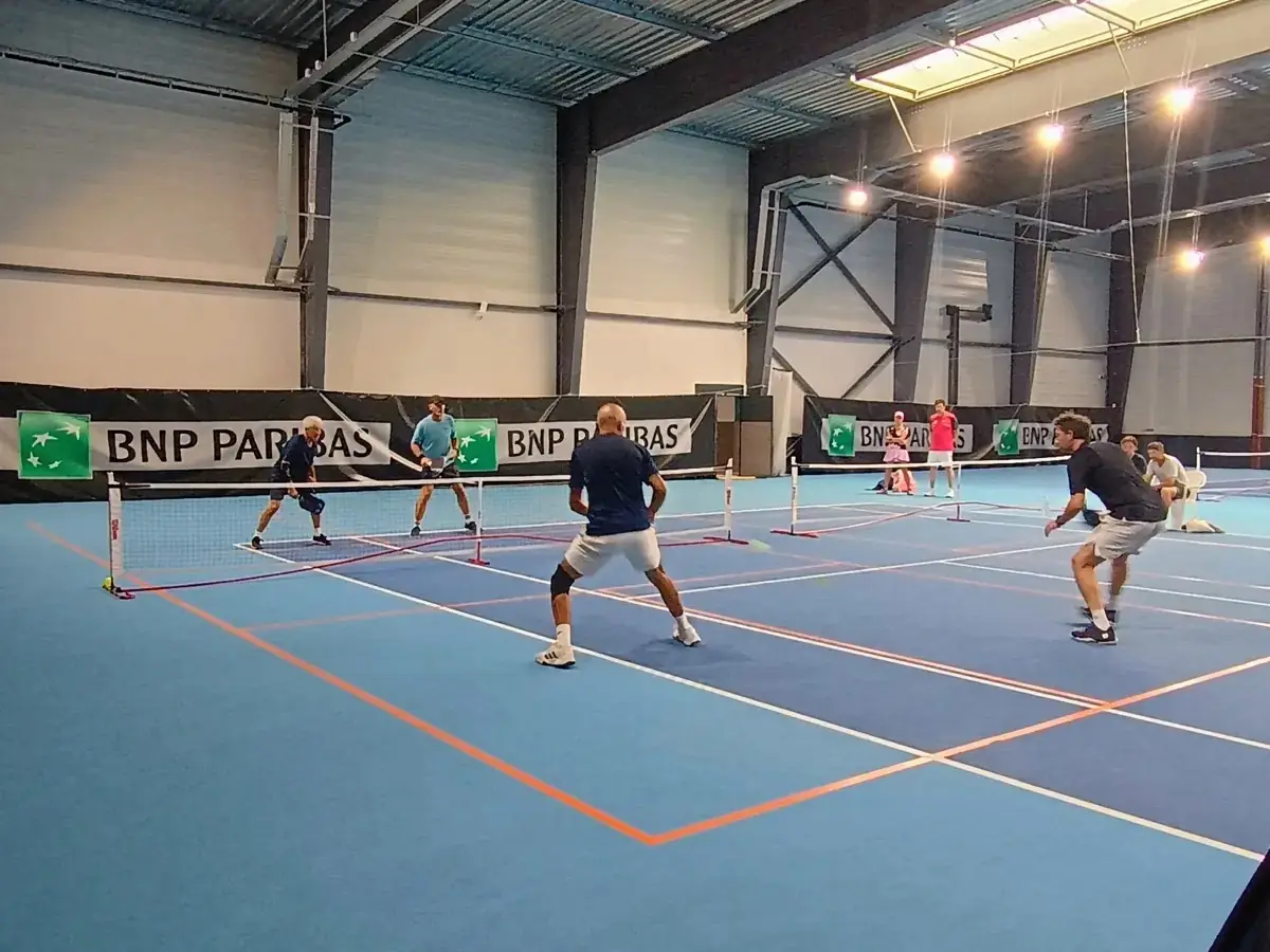 Point en cours sur un terrain intérieur des Championnats de France de pickleball 2026 avec joueur fléchi