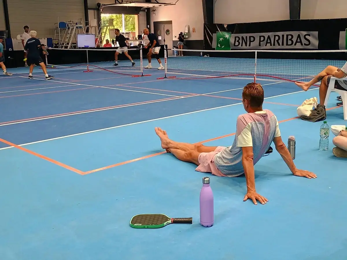 Joueuse assise au sol près d’un terrain intérieur des Championnats de France de pickleball 2026