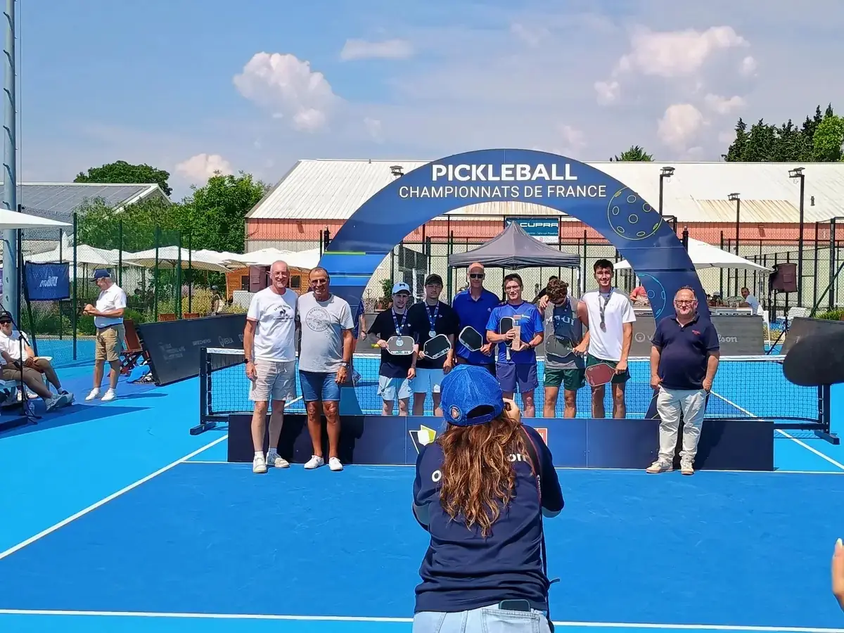 Photographe devant un groupe sous l’arche officielle des Championnats de France de pickleball 2026