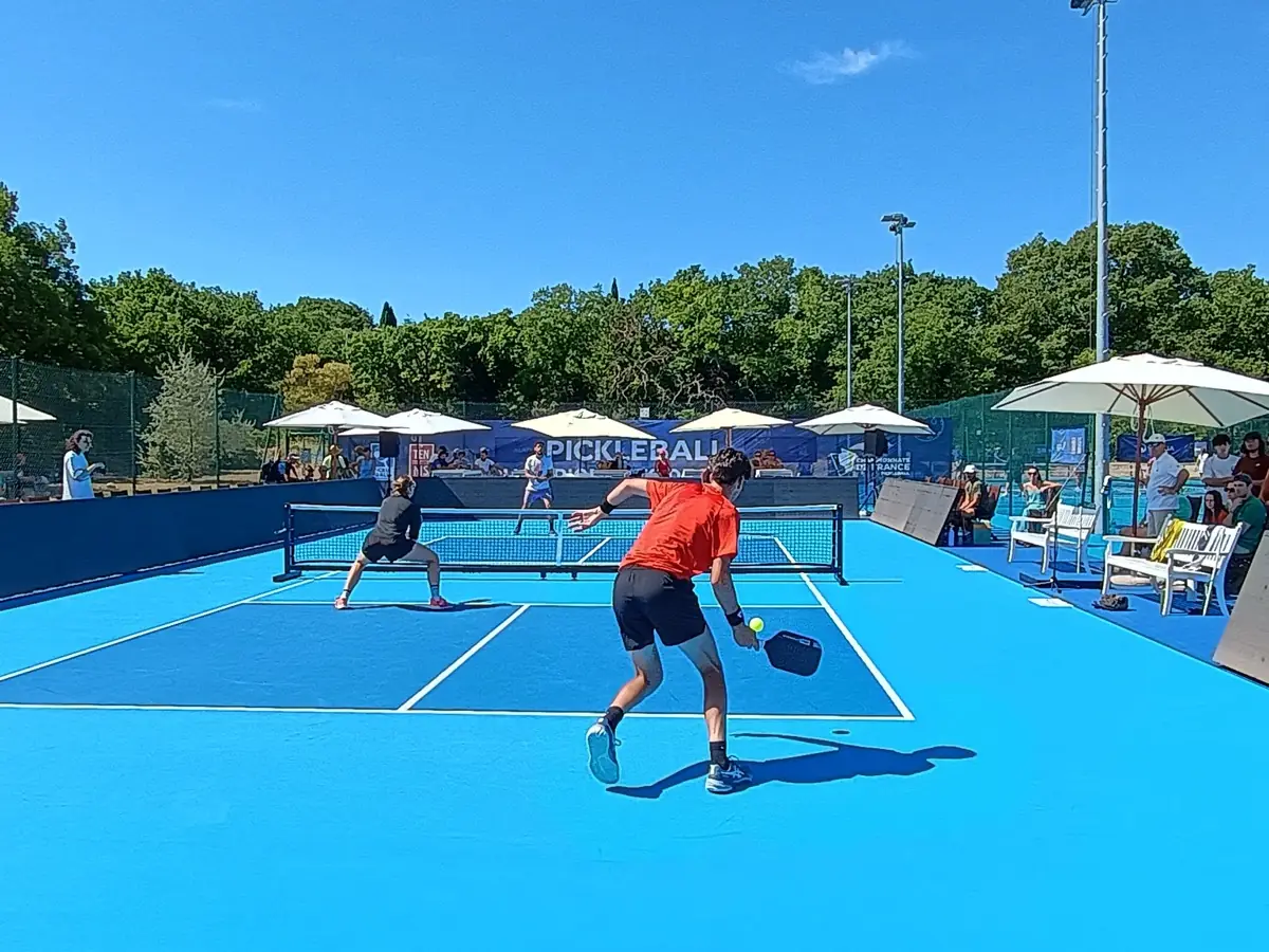 Joueur en rouge au filet pendant un échange sur les courts extérieurs des Championnats de France de pickleball 2026