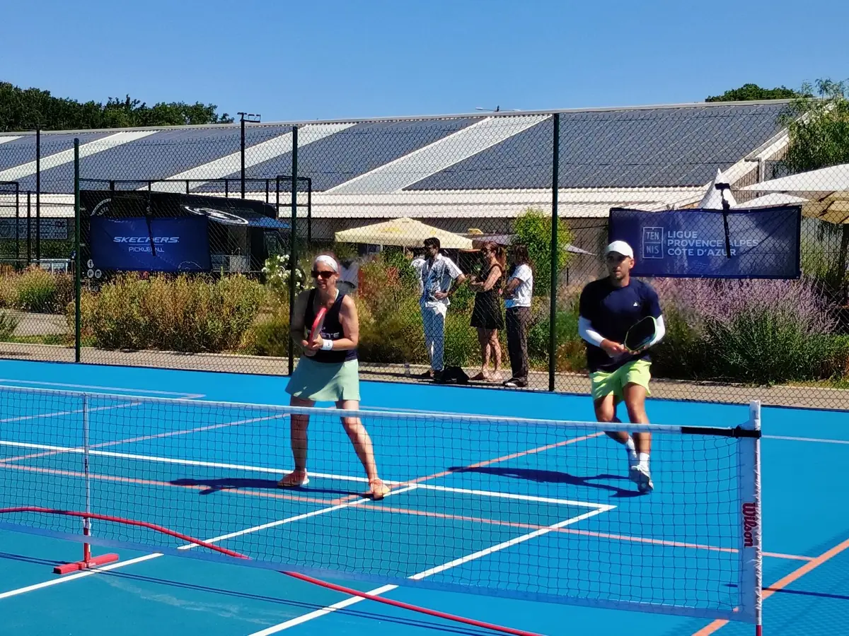 Échange en double avec deux joueuses au premier plan sur un terrain extérieur des Championnats de France de pickleball 2026