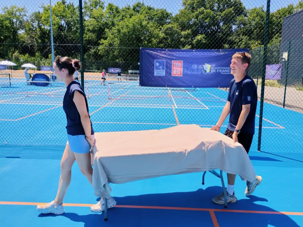 Deux personnes déplacent une table près des terrains extérieurs des Championnats de France de pickleball 2026