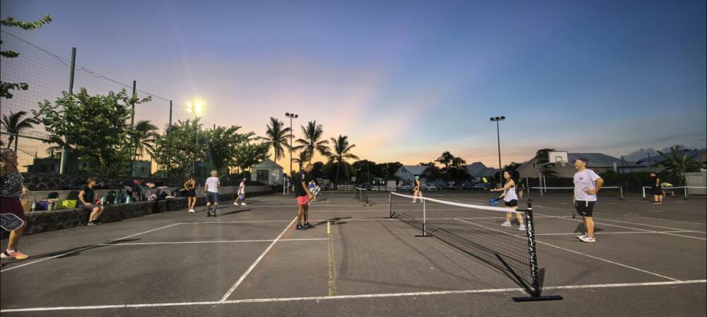 Joueuses et joueurs de pickleball sur plusieurs terrains extérieurs en soirée